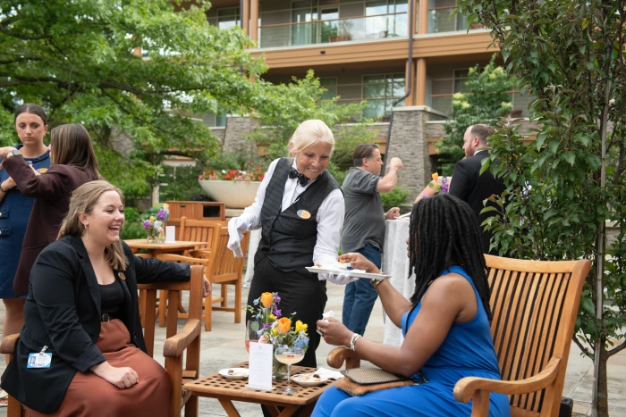 Outdoor gathering at Turning Stone with a server smiling while serving 2 women appetizers from a tray. 