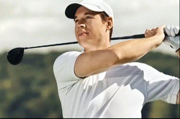 A male in a white polo swinging a golf club