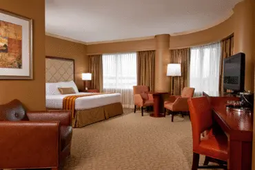 The romantic deluxe room at The Hotel at Turning Stone with an open floor plan, king bed, leather arm chair, and dining set